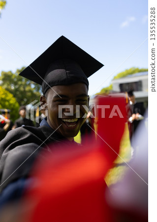 Teen graduate outdoors smiling and holding diploma during graduation ceremony Teen graduate outdoors smiling and holding diploma during graduation ceremony 135535288
