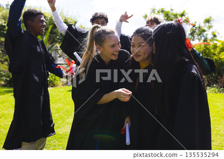 Graduating students celebrating outdoors, smiling and holding diplomas in excitement Graduating students celebrating outdoors, smiling and holding diplomas in excitement 135535294