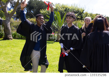 Graduating students holding diplomas and wearing caps, celebrating outdoors together Graduating students holding diplomas and wearing caps, celebrating outdoors together 135535296
