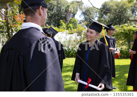 Graduating students in caps and gowns celebrating outdoors with diplomas in hand 135535301