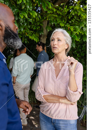 Mature woman in conversation with African American man at outdoor wedding event Mature woman in conversation with African American man at outdoor wedding event 135535427