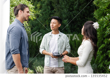 Celebrating wedding, friends conversing outdoors surrounded by lush greenery Celebrating wedding, friends conversing outdoors surrounded by lush greenery 135535452
