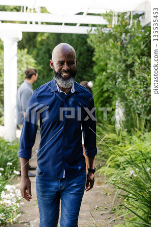 Smiling African American man walking through garden at wedding celebration 135535453