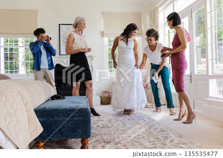 Bride in white dress surrounded by friends, preparing for wedding ceremony at home Bride in white dress surrounded by friends, preparing for wedding ceremony at home 135535477
