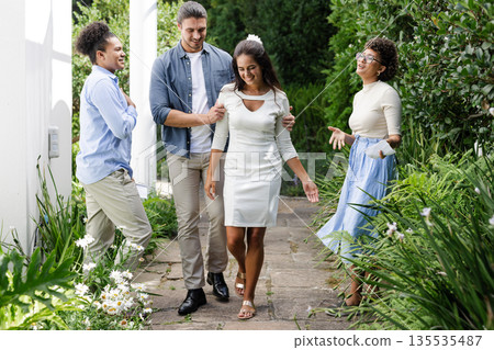 Friends joyfully walking with bride in garden, celebrating wedding day together 135535487