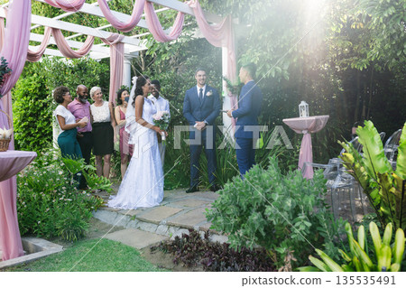 Bride and groom exchanging vows outdoors surrounded by family and friends Bride and groom exchanging vows outdoors surrounded by family and friends 135535491