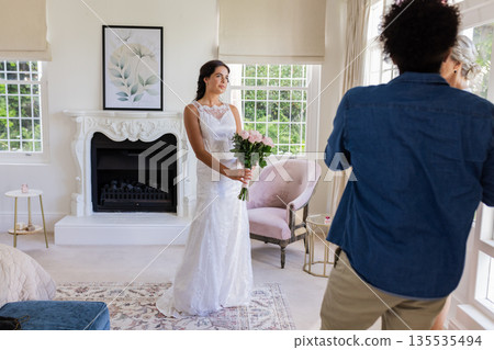 Holding bouquet, bride smiling as photographer captures moment in elegant room Holding bouquet, bride smiling as photographer captures moment in elegant room 135535494