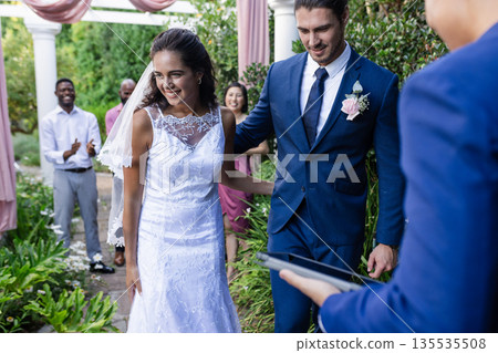 Bride and groom walking down aisle, smiling joyfully at outdoor wedding ceremony 135535508