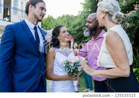Bride and groom smiling with guests, celebrating joyful wedding day outdoors 135535515
