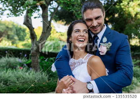 Bride and groom embracing joyfully in lush garden, celebrating their wedding day Bride and groom embracing joyfully in lush garden, celebrating their wedding day 135535520