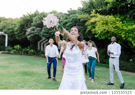 Bride joyfully tossing bouquet to excited guests in lush garden setting Bride joyfully tossing bouquet to excited guests in lush garden setting 135535525
