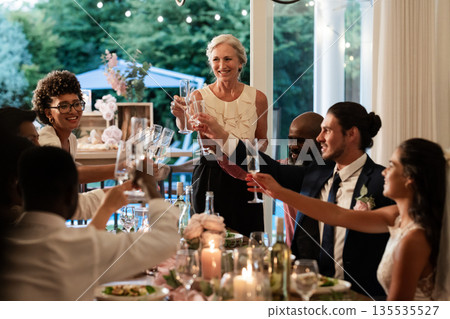 Guests raising glasses in joyful toast at elegant wedding reception dinner 135535527