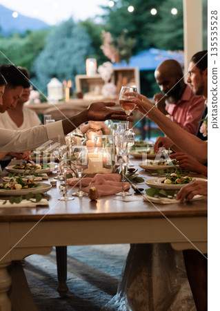 Guests toasting with wine glasses at elegant outdoor wedding dinner table 135535528