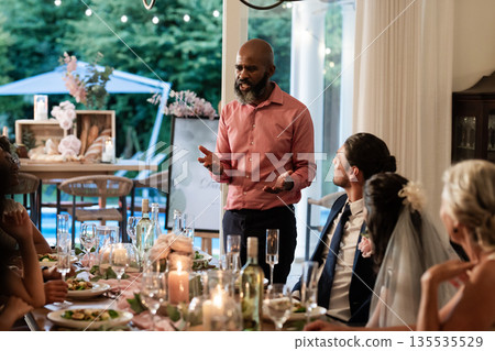At wedding reception, man giving heartfelt speech, guests listening attentively around table 135535529