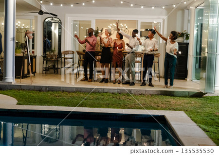 Friends celebrating with sparklers by poolside at evening wedding reception 135535530