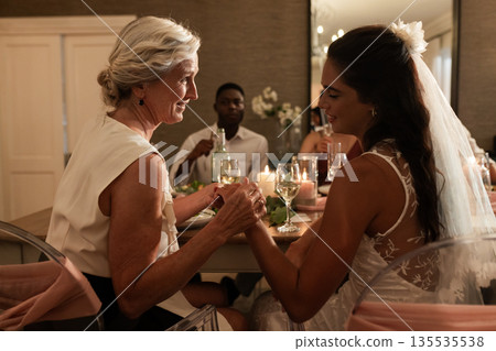 Bride holding hands with elderly woman, sharing heartfelt moment at reception 135535538