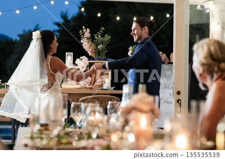 Bride and groom dancing joyfully at outdoor wedding reception under string lights 135535539