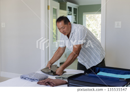 Packing suitcase, senior man folding clothes at home, preparing for travel Packing suitcase, senior man folding clothes at home, preparing for travel 135535547