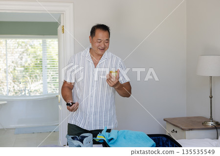 Packing suitcase at home, man holding smartphone during travel preparations Packing suitcase at home, man holding smartphone during travel preparations 135535549