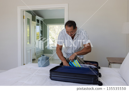 Asian man packing suitcase on bed in bedroom, preparing for travel Asian man packing suitcase on bed in bedroom, preparing for travel 135535550