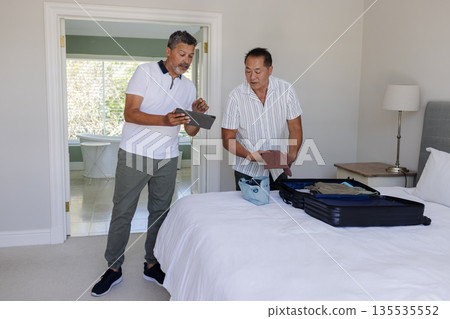 Senior men packing suitcase together in bedroom, preparing for travel 135535552