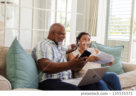 African American couple celebrating with smartphone and documents on sofa at home African American couple celebrating with smartphone and documents on sofa at home 135535571