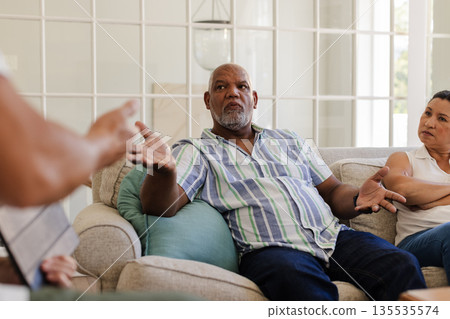 Senior man in striped shirt discussing with friends on sofa at home Senior man in striped shirt discussing with friends on sofa at home 135535574