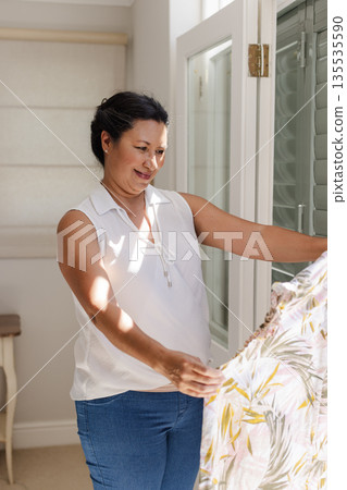 Smiling woman admiring floral dress at home, enjoying peaceful afternoon 135535590