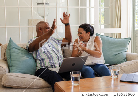 Senior couple celebrating success at home with laptop, smiling and clapping Senior couple celebrating success at home with laptop, smiling and clapping 135535600