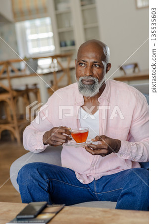 Senior man enjoying tea at home, relaxing in comfortable living room chair 135535603