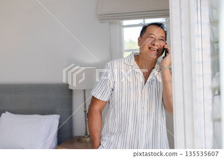 Asian man talking on smartphone at home, smiling and looking relaxed 135535607