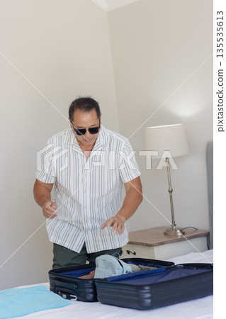 Senior man packing suitcase at home, preparing for travel with sunglasses on Senior man packing suitcase at home, preparing for travel with sunglasses on 135535613