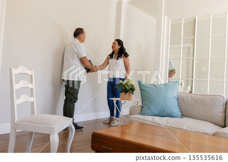 Smiling couple shaking hands in living room, celebrating successful home purchase Smiling couple shaking hands in living room, celebrating successful home purchase 135535616
