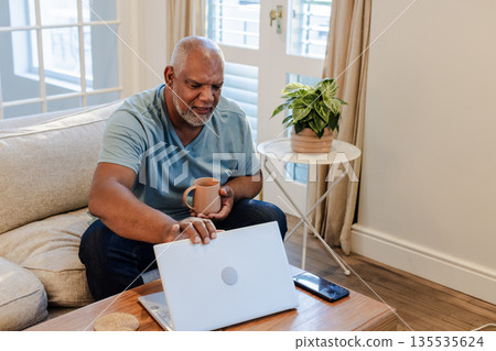 Senior man relaxing at home with laptop and coffee, enjoying leisure time 135535624