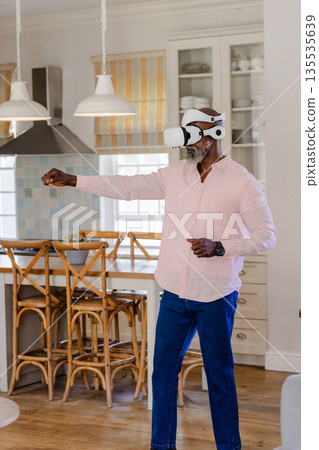 Senior man using VR headset in kitchen, engaging in virtual reality experience 135535639