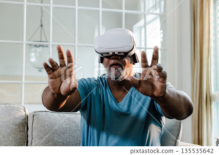African American man using VR headset on sofa, exploring virtual reality experience 135535642