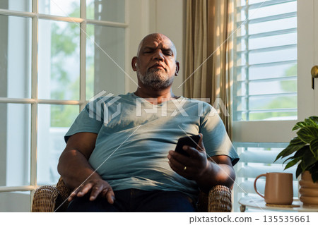 Senior man relaxing at home, holding remote control, enjoying quiet evening 135535661