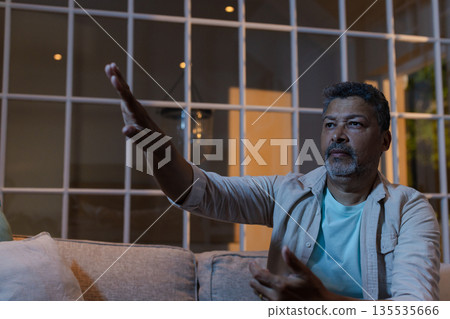 Senior man gesturing enthusiastically while sitting on sofa at home in evening 135535666