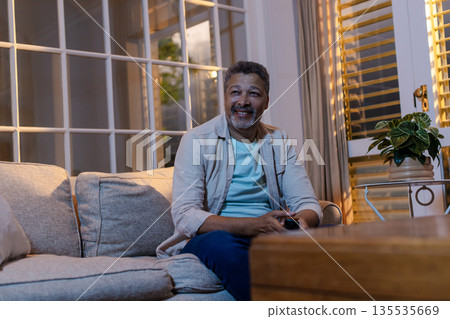 African American man relaxing on sofa at home, smiling and watching television 135535669