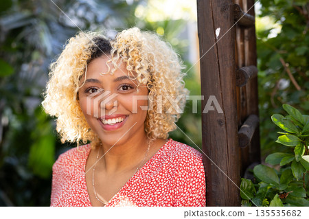 Smiling woman with curly hair enjoying sunny day in lush garden setting Smiling woman with curly hair enjoying sunny day in lush garden setting 135535682