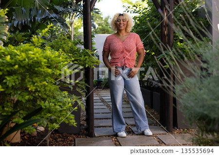 Smiling woman standing confidently in lush garden, enjoying sunny day outdoors Smiling woman standing confidently in lush garden, enjoying sunny day outdoors 135535694