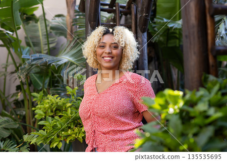 Smiling woman in red blouse enjoying nature surrounded by lush green plants 135535695