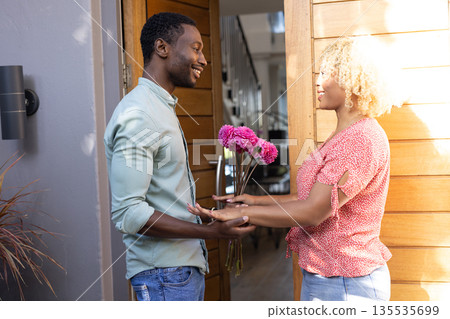 Man giving pink flowers to smiling woman at home entrance, sharing joyful moment Man giving pink flowers to smiling woman at home entrance, sharing joyful moment 135535699