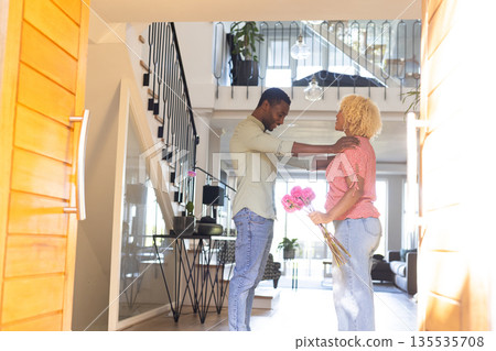 Young man giving flowers to woman in modern home, both smiling warmly Young man giving flowers to woman in modern home, both smiling warmly 135535708