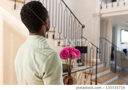 Man holding pink flowers, standing in elegant home, preparing surprise gesture 135535716