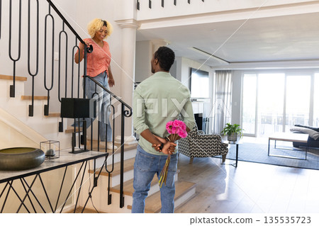 Man surprising woman with flowers at home, standing on staircase, smiling warmly Man surprising woman with flowers at home, standing on staircase, smiling warmly 135535723