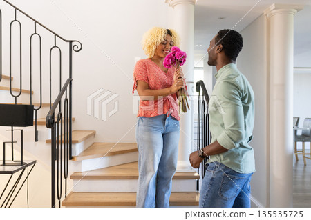 Smiling woman on stairs receiving flowers from friend in modern home 135535725