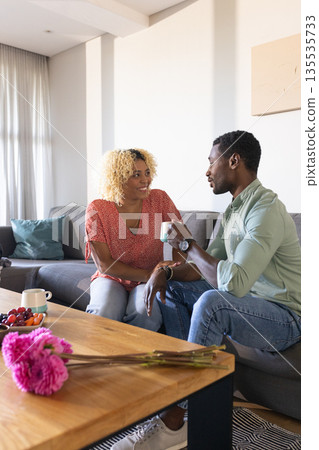 African American friends enjoying coffee and conversation on cozy living room sofa African American friends enjoying coffee and conversation on cozy living room sofa 135535733