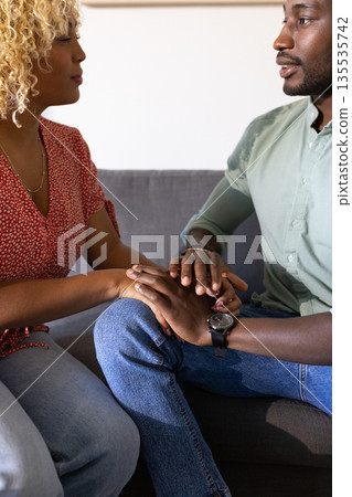 African American friends sitting on couch holding hands, sharing supportive moment 135535742