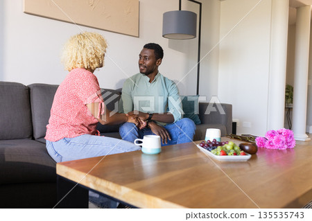 African American friends sitting on sofa, talking and enjoying coffee at home 135535743